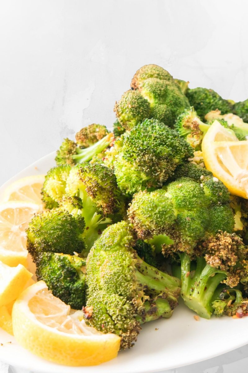 A serving platter of crispy air fryer broccoli with lemon wedges. 