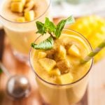Mango smoothies on a wooden board, garnished with mint and fresh mango.
