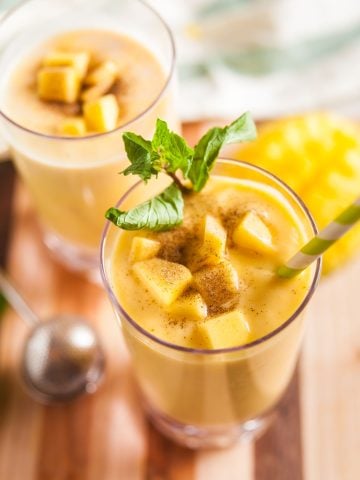 Mango smoothies on a wooden board, garnished with mint and fresh mango.