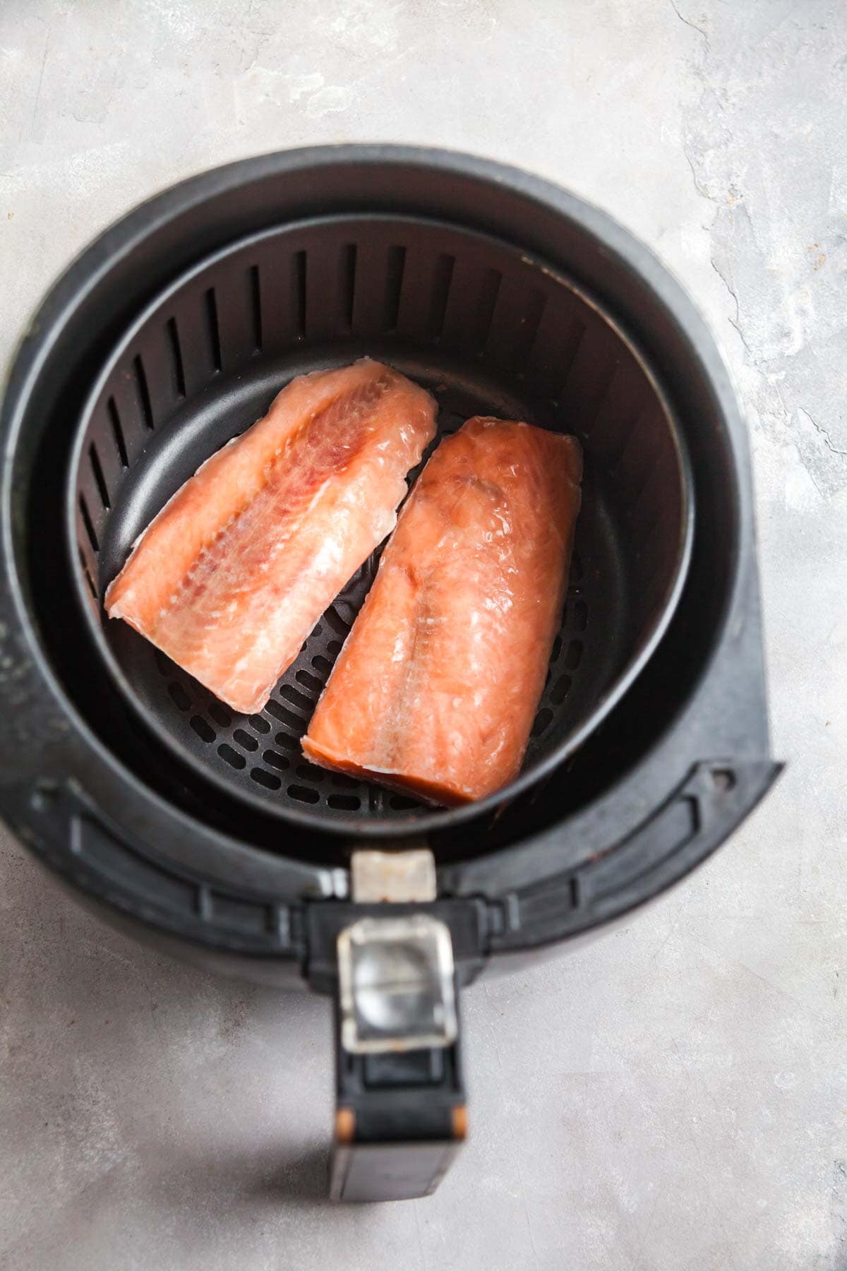 An overhead view of frozen salmon in an air fryer basket. 