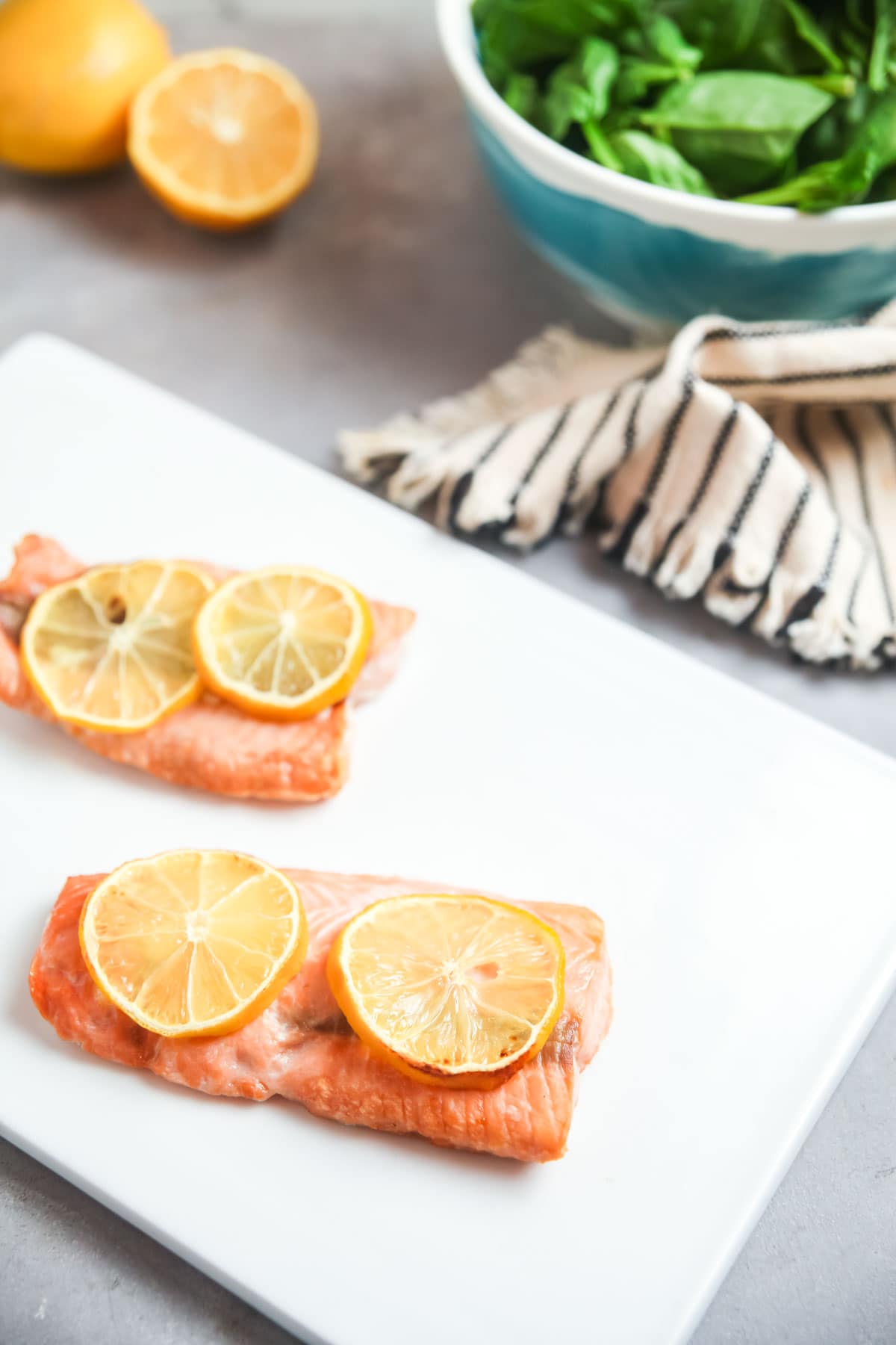 Air fryer frozen salmon fillets topped with lemon slices on a white board.