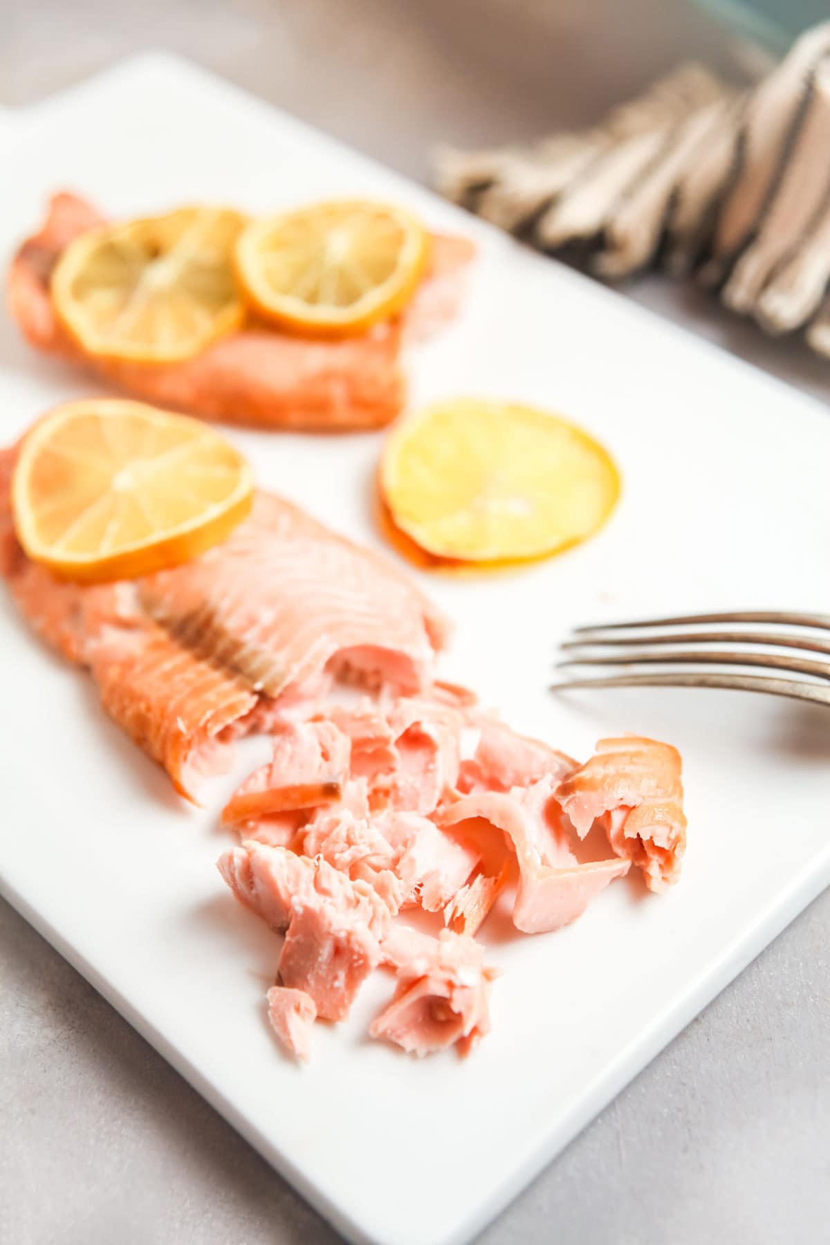 An air fried frozen salmon fillet on a white cutting board, with a fork showing how tender and flaky the cooked fish is. 