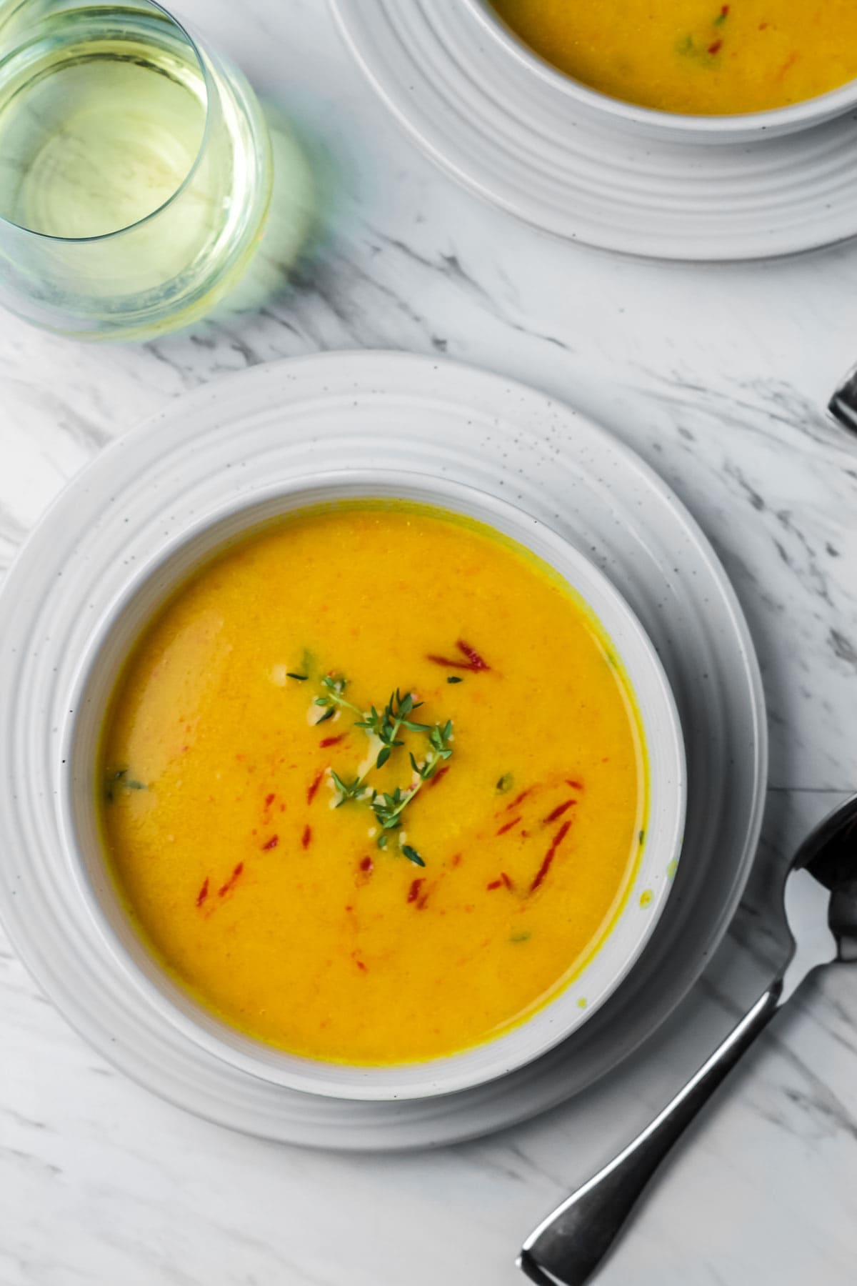 An overhead view of a bowl of curried butternut squash soup on a white marble background with a glass of white wine beside it. 