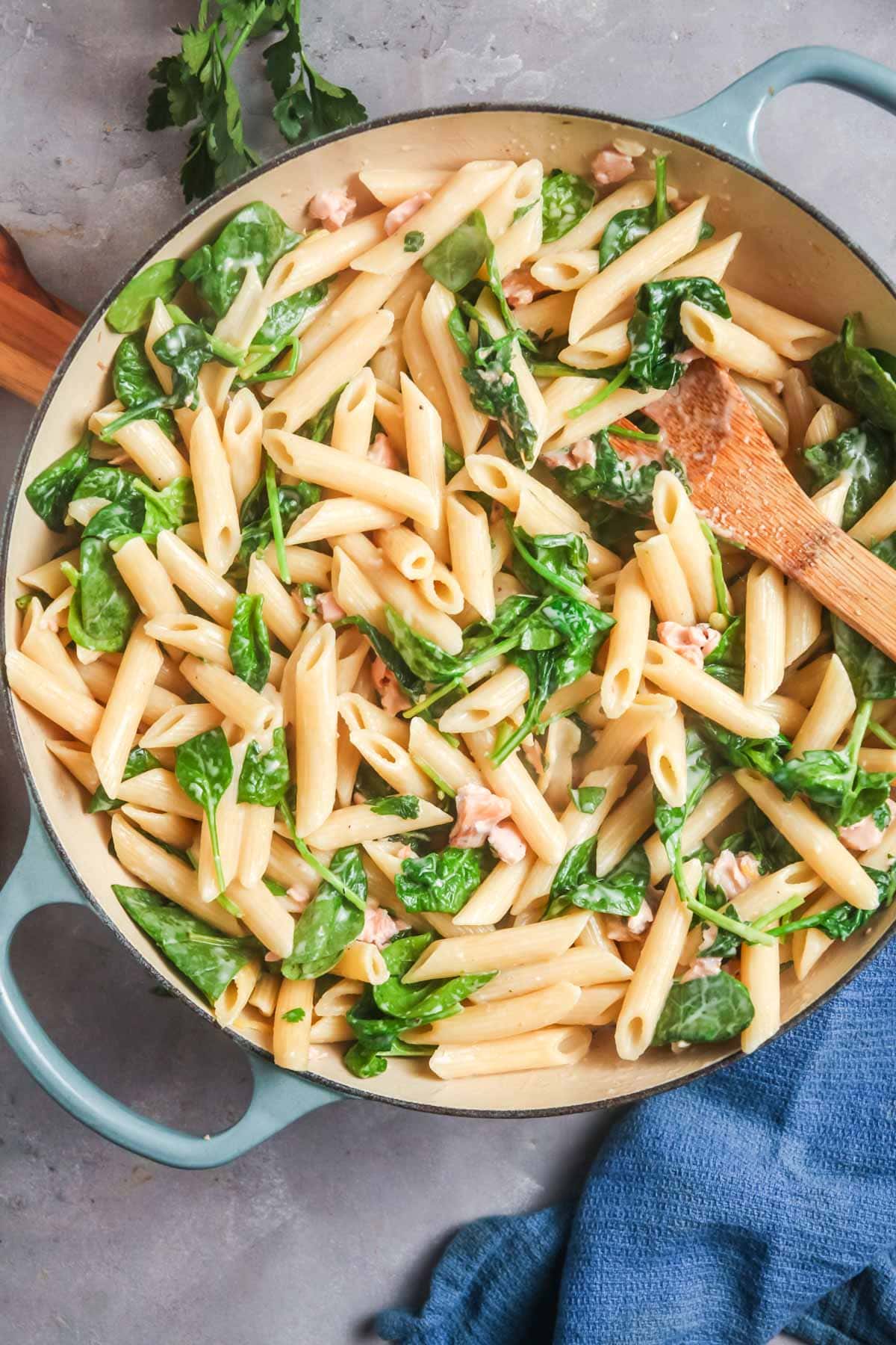 An overhead view of salmon pasta with spinach and cream sauce  in a wide blue pan.