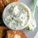 A dish of tzatziki sauce with zucchini fritters.