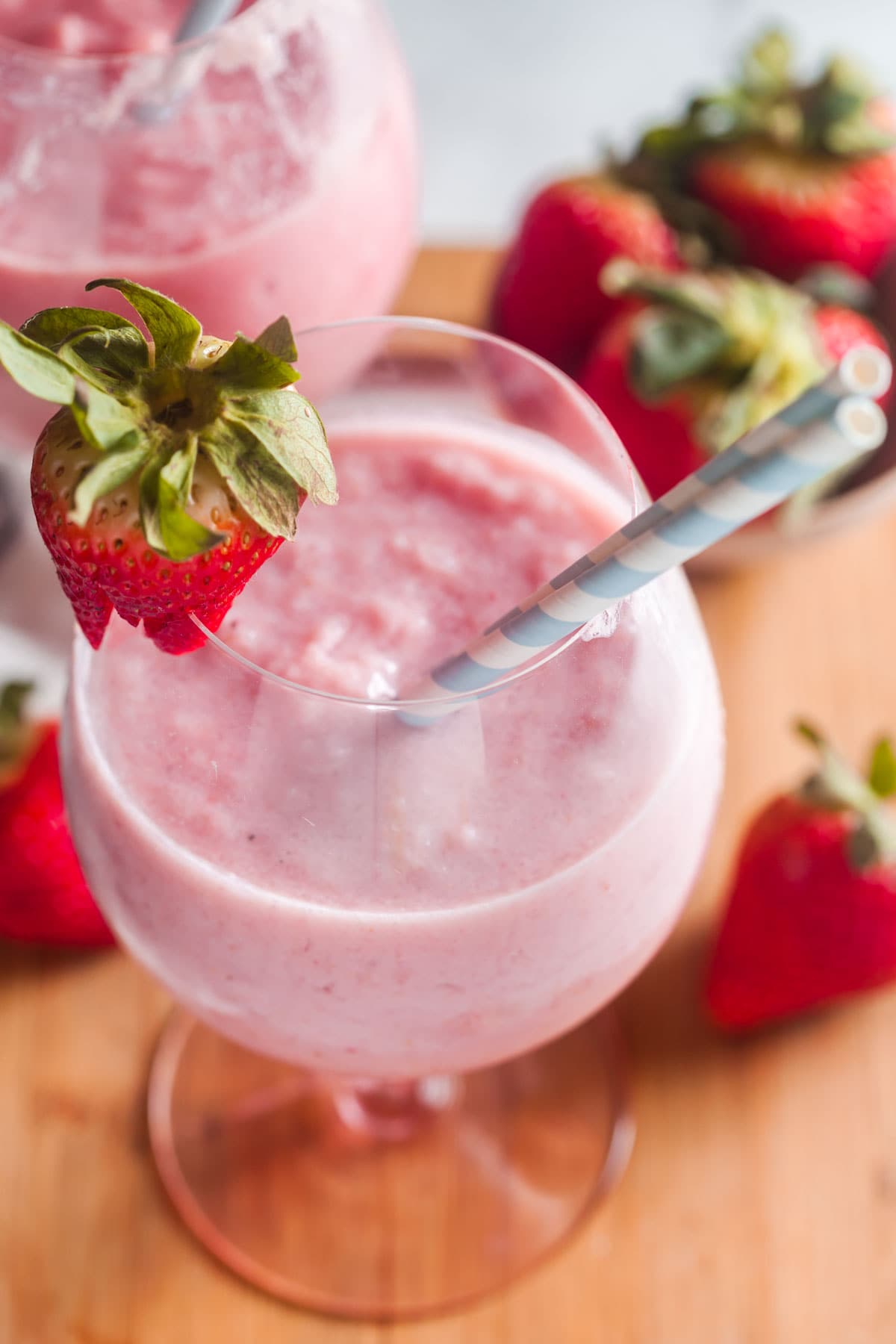 A closeup view of two large glasses filled with strawberry banana smoothies. Garnished with fresh berries and stirpy straws. 