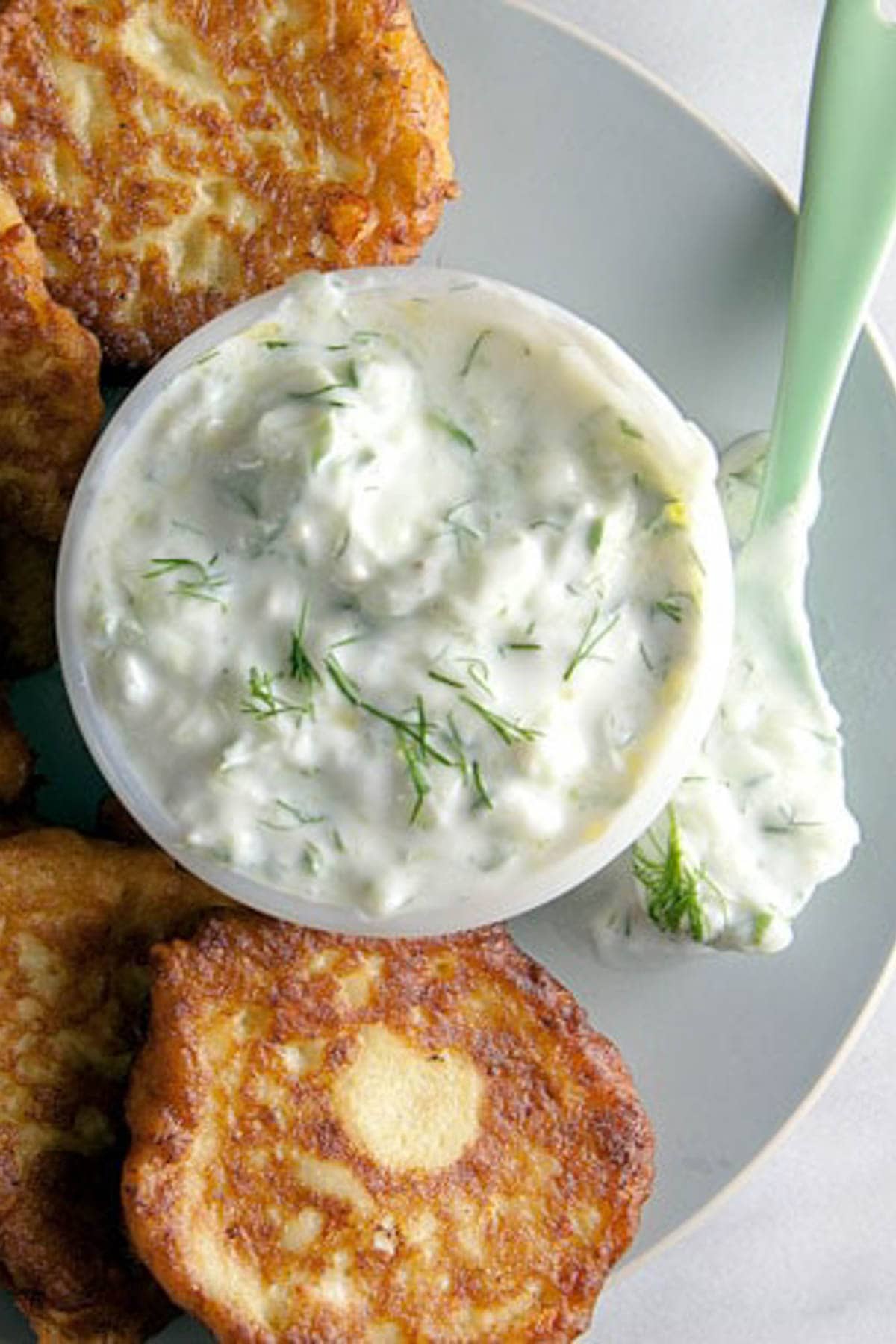 Overhead shot of a grey plate with zucchini fritters and a dish of homemade tzatziki sauce. 