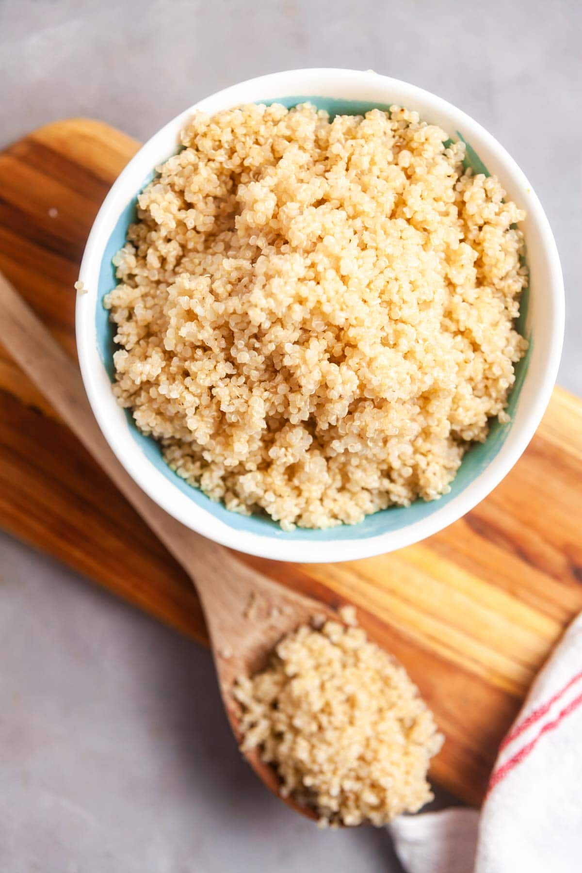 Overhead view of a bowl of quinoa on a wooden serving board. A spoon of quinoa is in front of the bowl. 