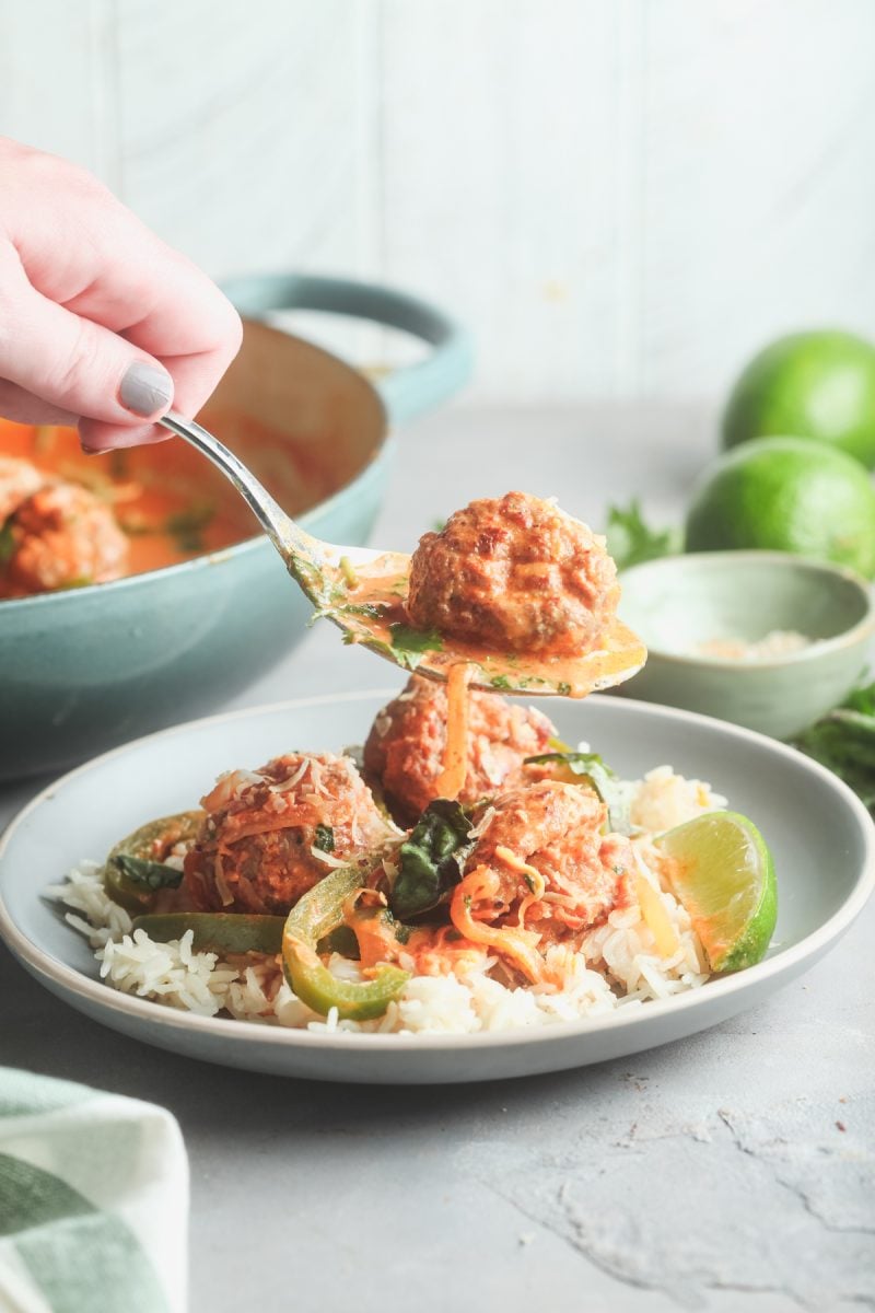 Spooning up a serving of Thai curry meatballs onto a plate. 