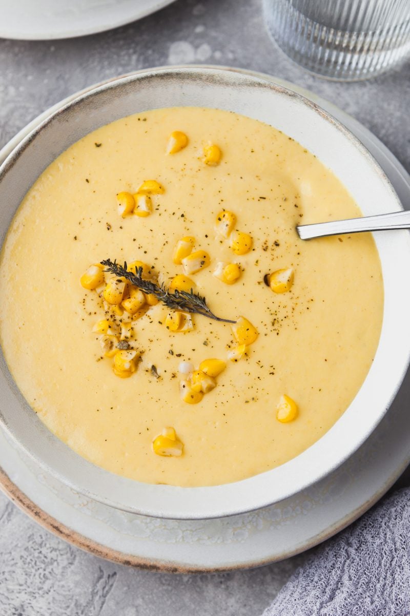 Close up overhead view of a bowl of creamy corn chowder topped with fresh corn and thyme. 