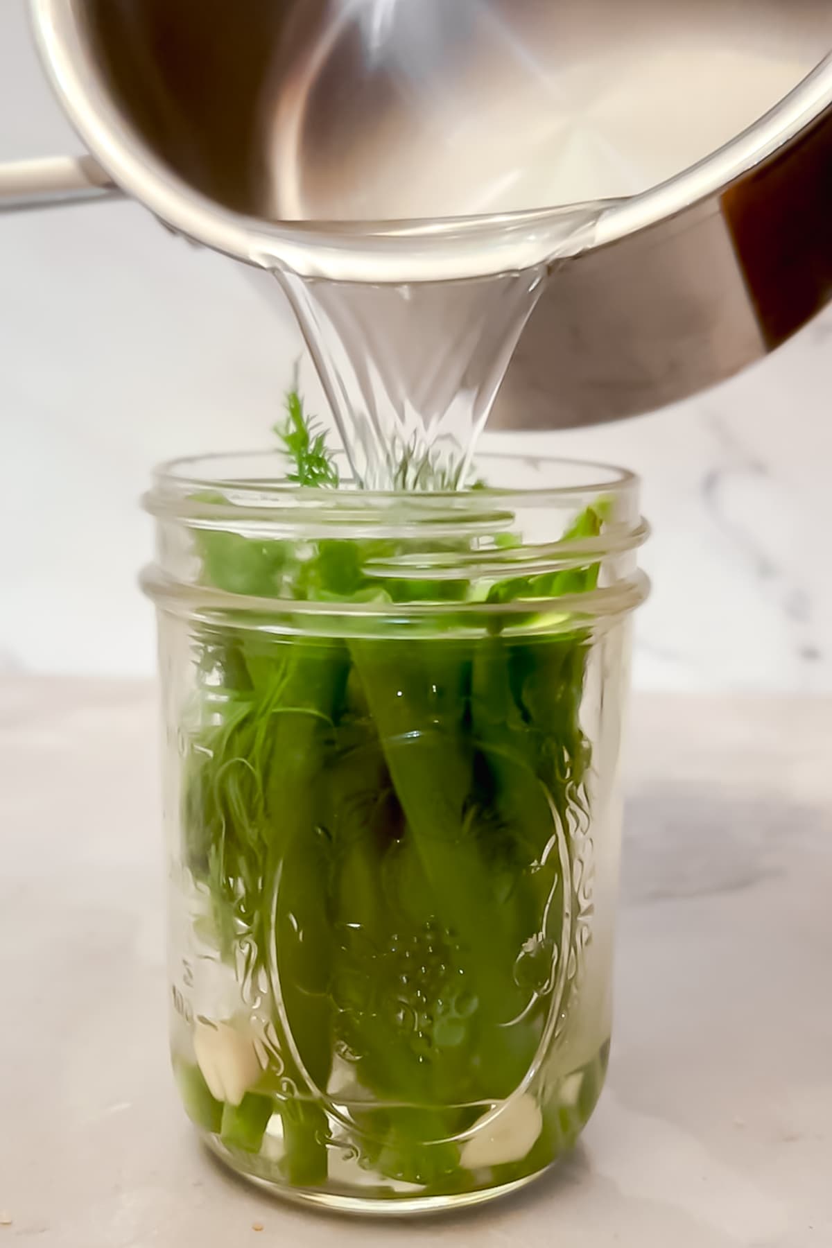 Pouring the brine into a jar of pickled green beans. 