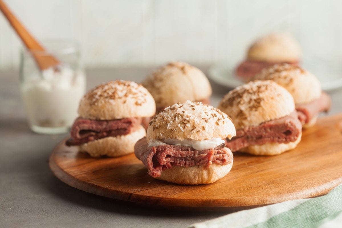 Landscape image of beef on weck sandwiches with horseradish spread in the background.