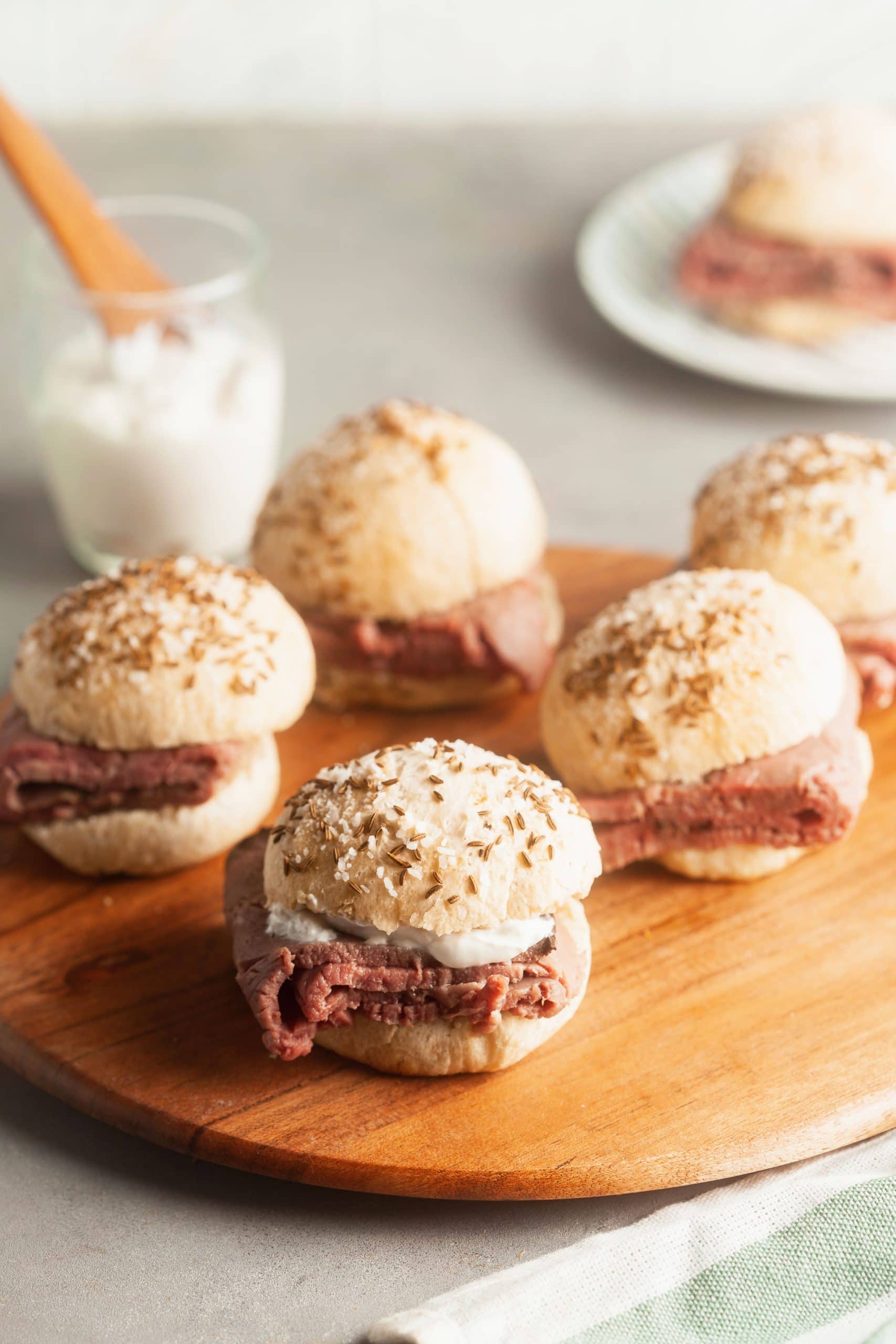 A wooden serving board with beef on weck sandwiches and horseradish. 