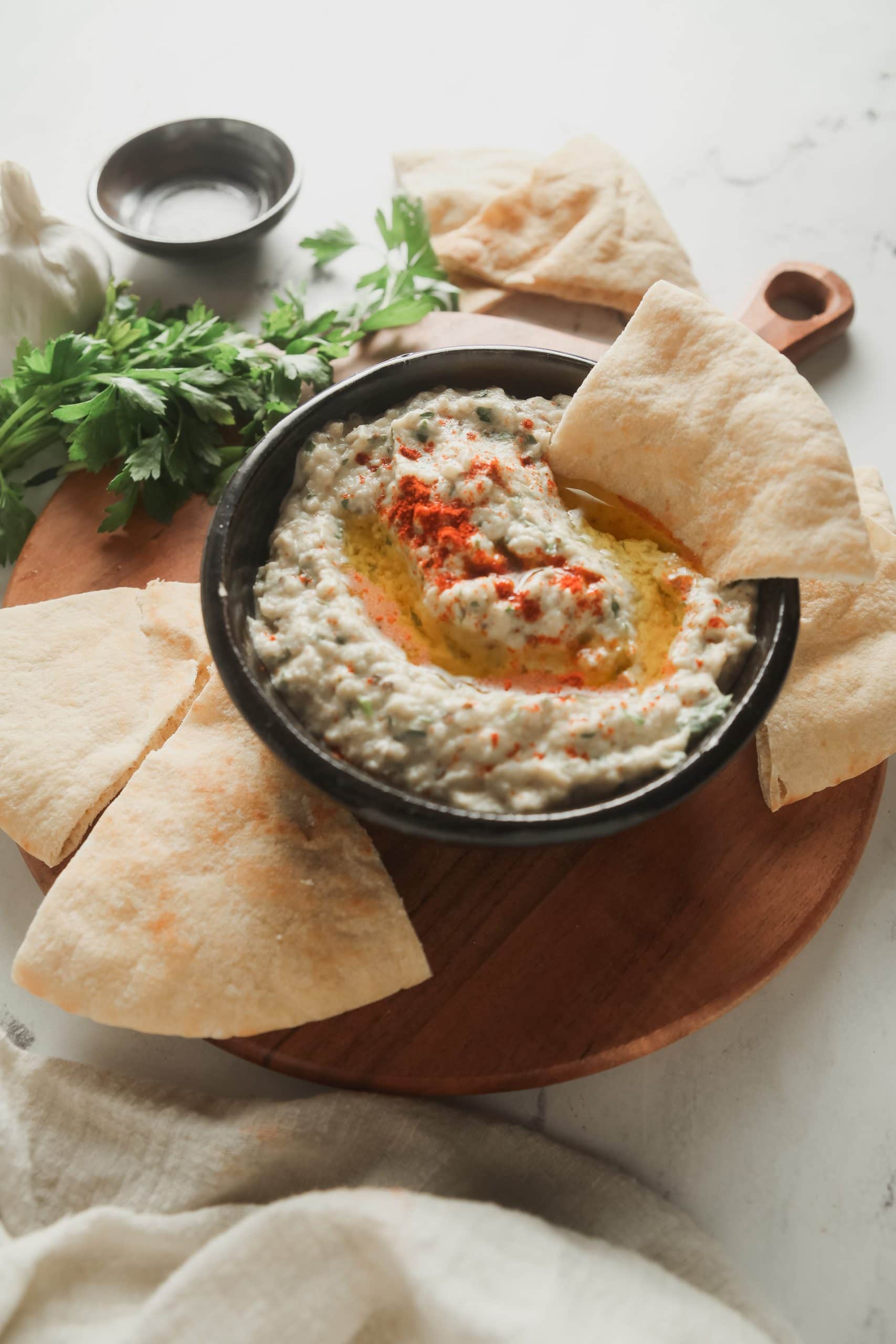 A curring board with a bowl of baba ganoush and pita wedges. 