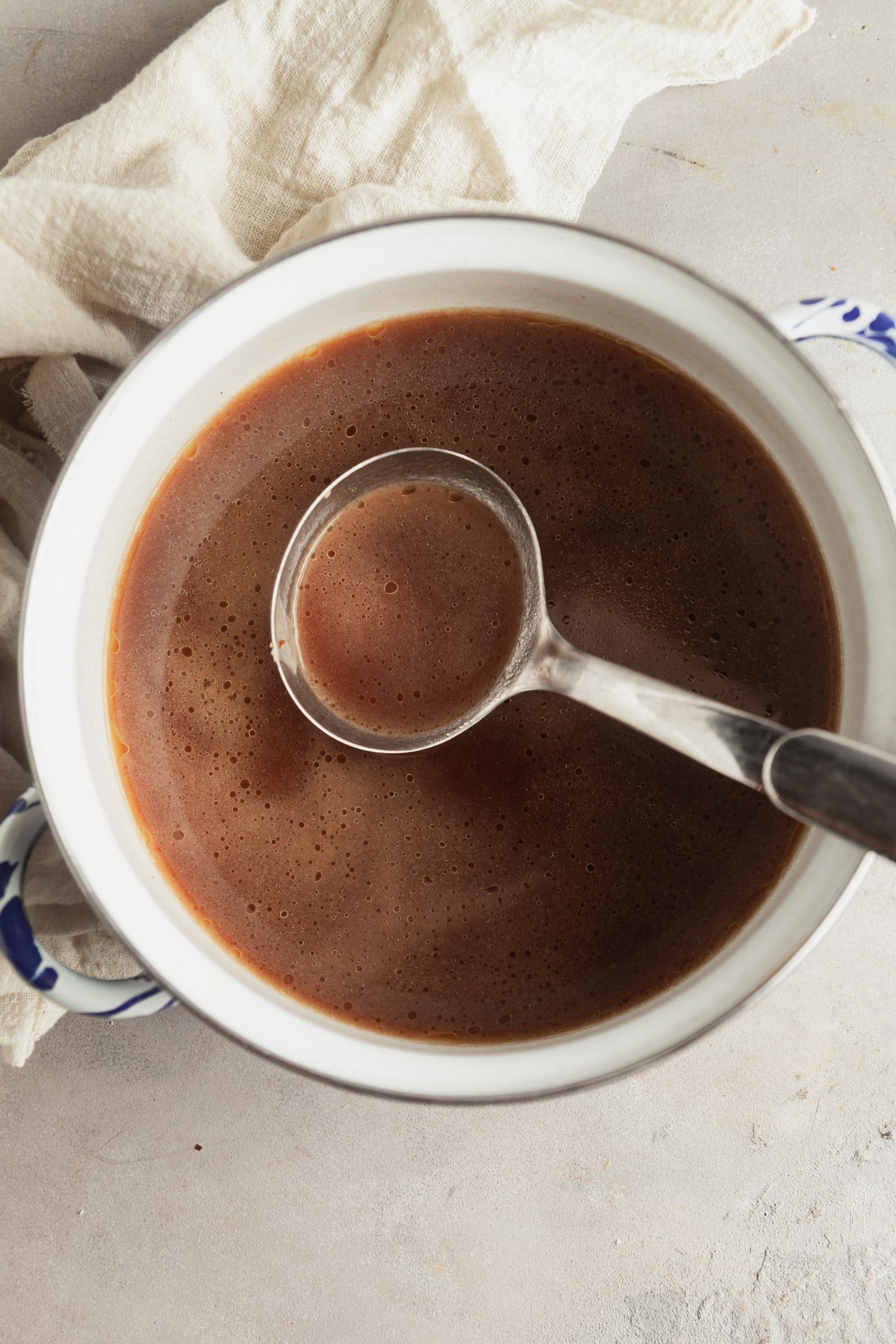 A pot full of au jus sauce with a ladle.