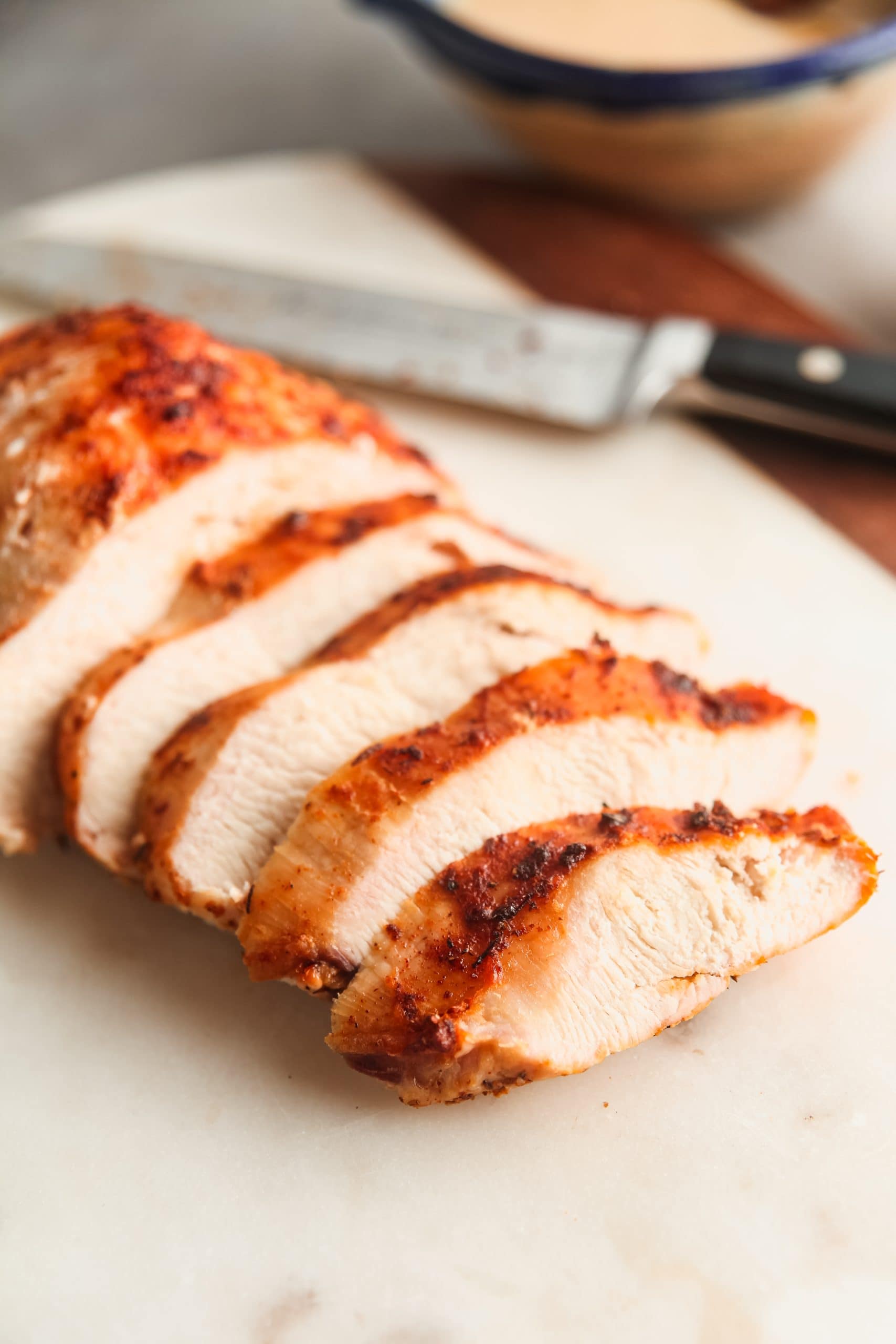 How to cook frozen chicken in the air fryer: Juicy air fryer chicken breast, sliced on a white cutting board.
