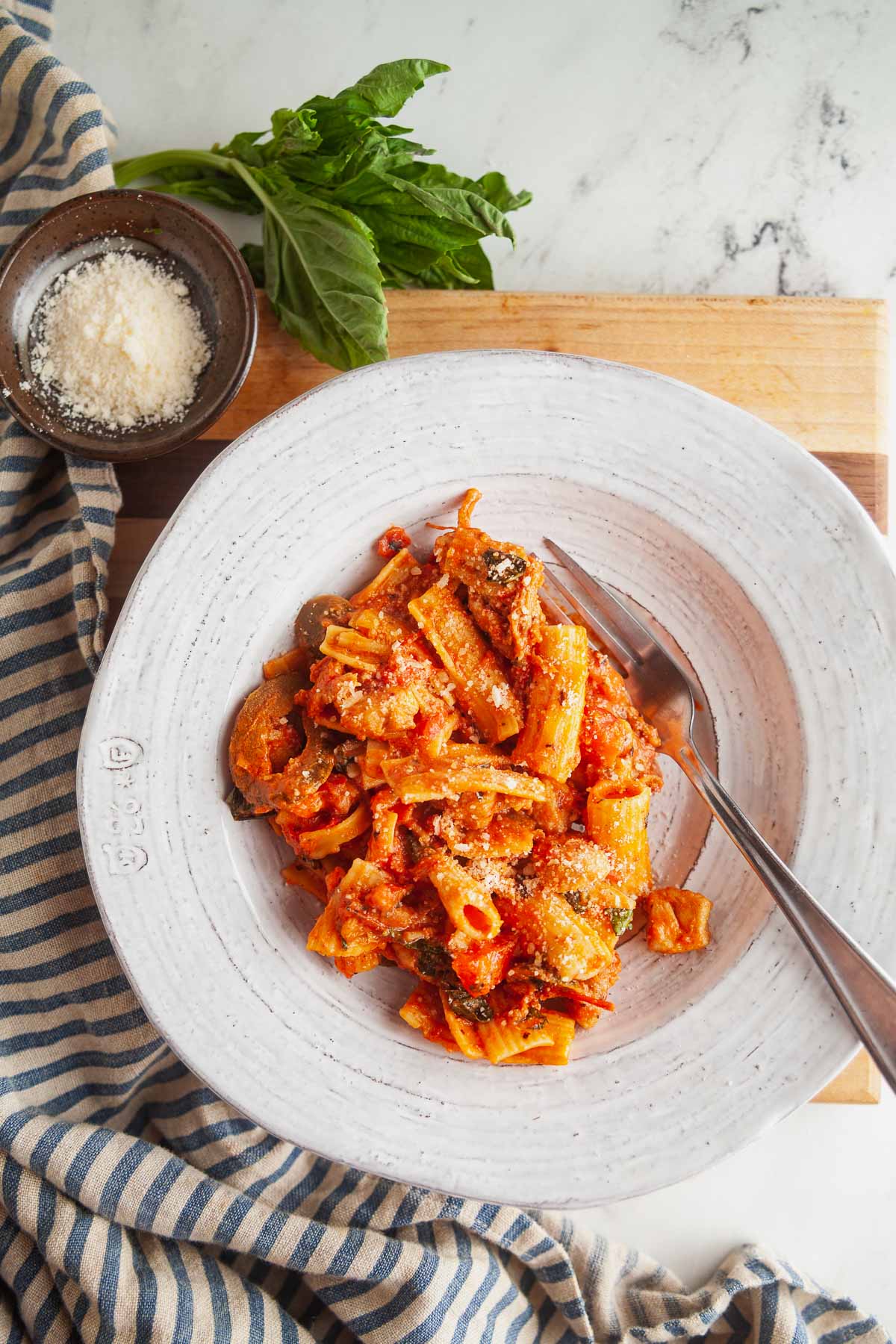 An overhead view of Utica chicken riggies in a white dish, with garlic and basil in the background. 