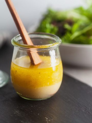 Basic vinaigrette in a small glass jar with a wooden spoon.