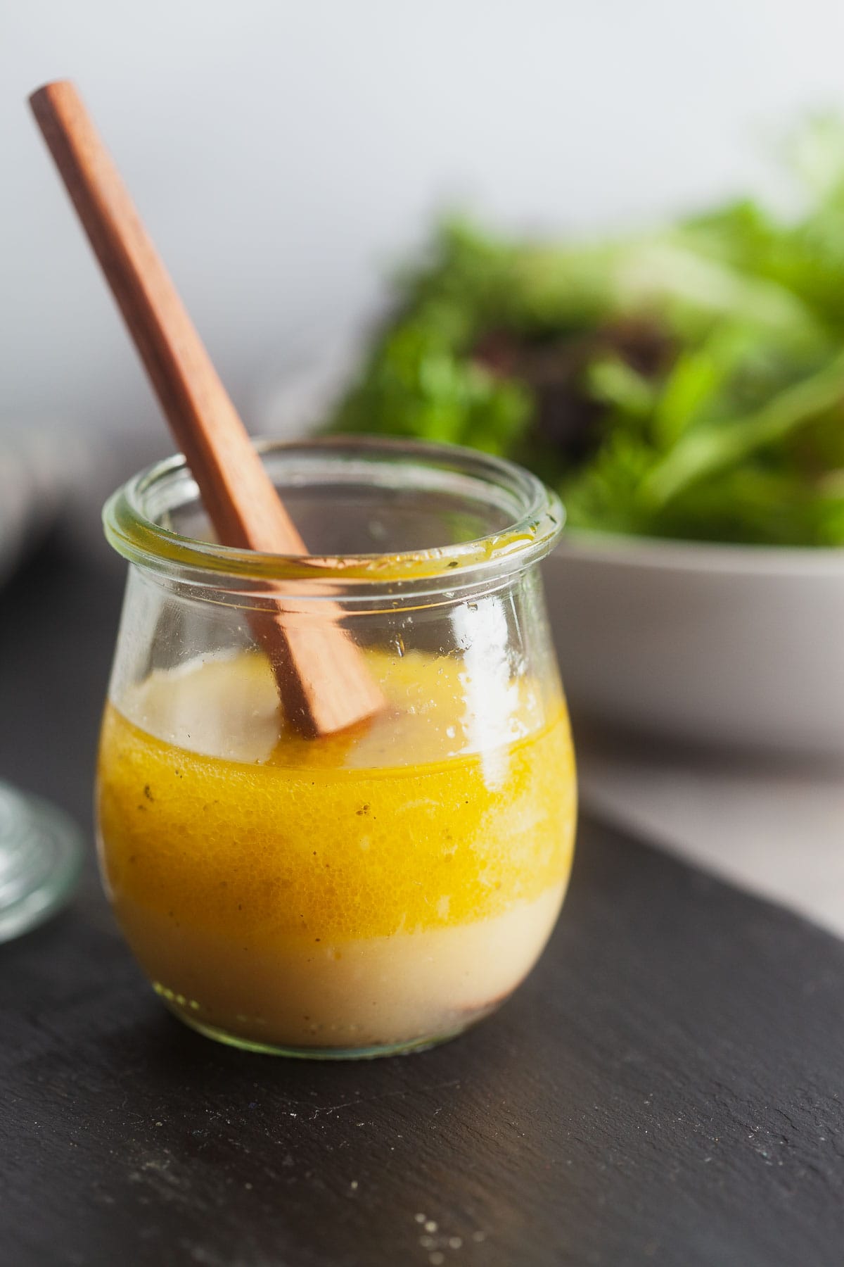 Basic vinaigrette in a small glass jar with a wooden spoon. 