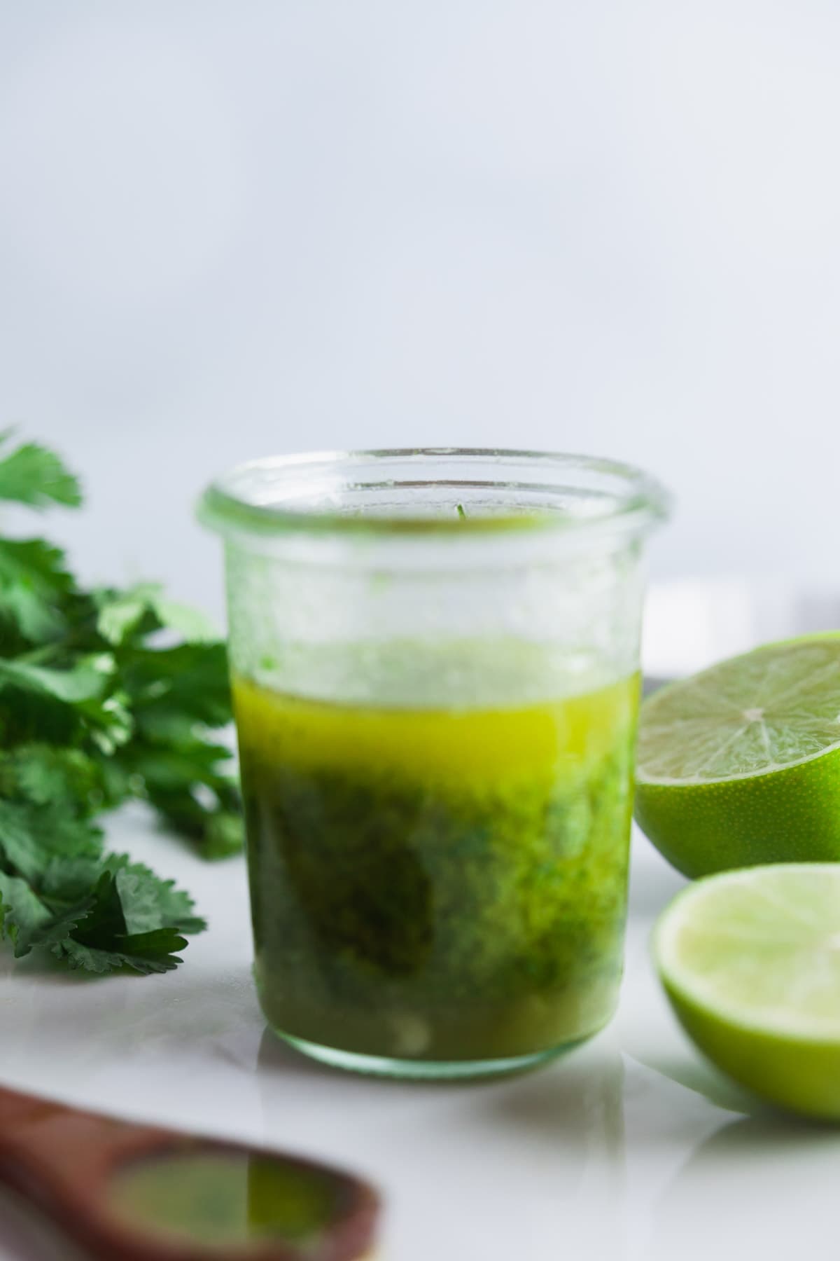 A small glass jar of cilantro-lime dressing on a white porcelain surface. 