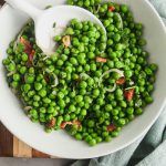Close up image of peas with mint in a white bowl with a serving spoon.