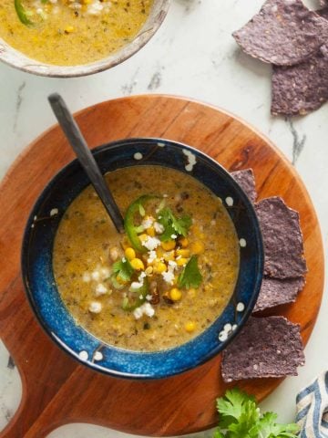 Overhead view of a bowl of Mexican street corn chowder, garnished with blue corn tortilla chips.