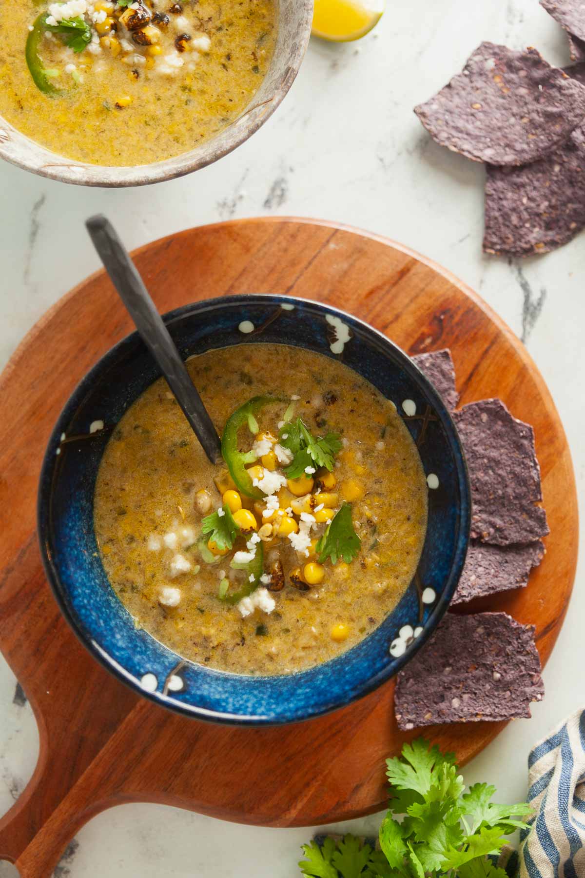 Overhead view of a bowl of Mexican street corn chowder, garnished with blue corn tortilla chips. 