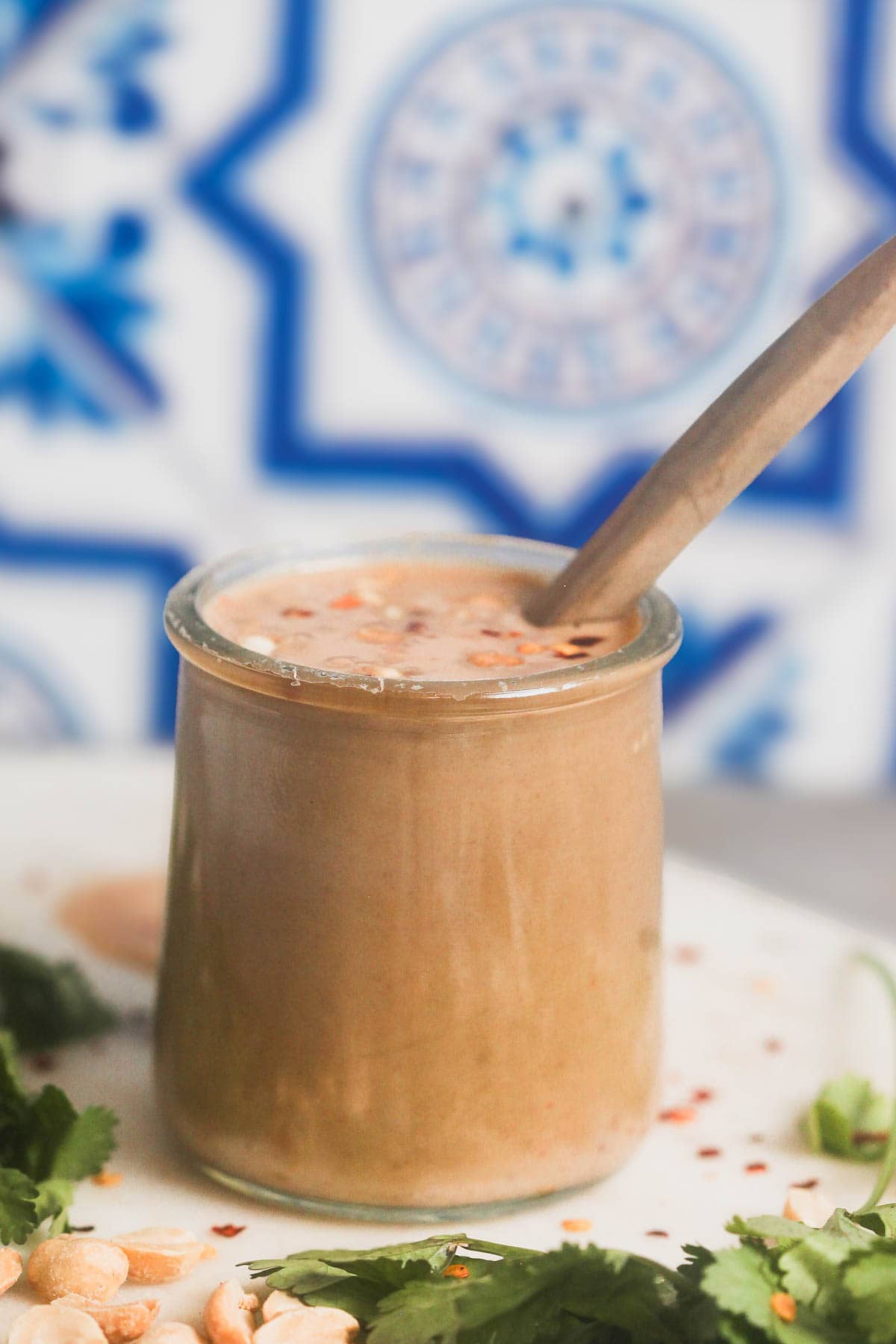 A small glass jar filled with homemade peanut sauce against a blue tile background. 