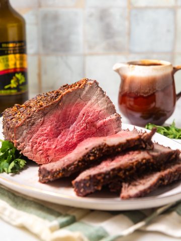 Medium-rare air fryer roast beef on a white platter with wine and gravy in the background.